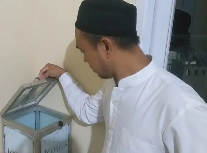 DIBOBOL–Ketua DKM Musala Al-Muqodas, Ustaz Maman sedang menujukan kondisi kotak amal usai dibobol maling, Senin (18/4/2022). (NIPAL SUTIANA/SATELITNEWS.ID)