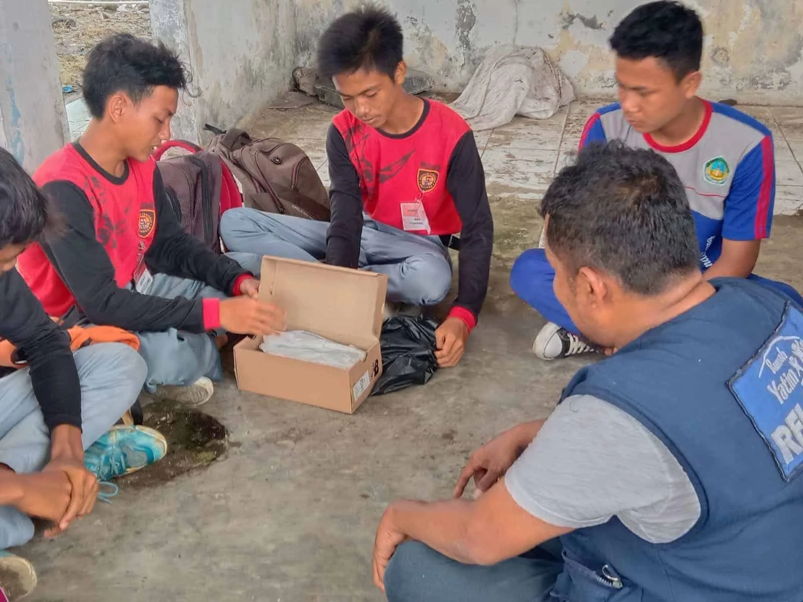 Giwan, didampingi teman-temannya sedang membuka dus untuk melihat sepasang sepatu, yang diberikan relawan Laznas Rumah Yatim, Senin (18/7/2022). (ISTIMEWA)