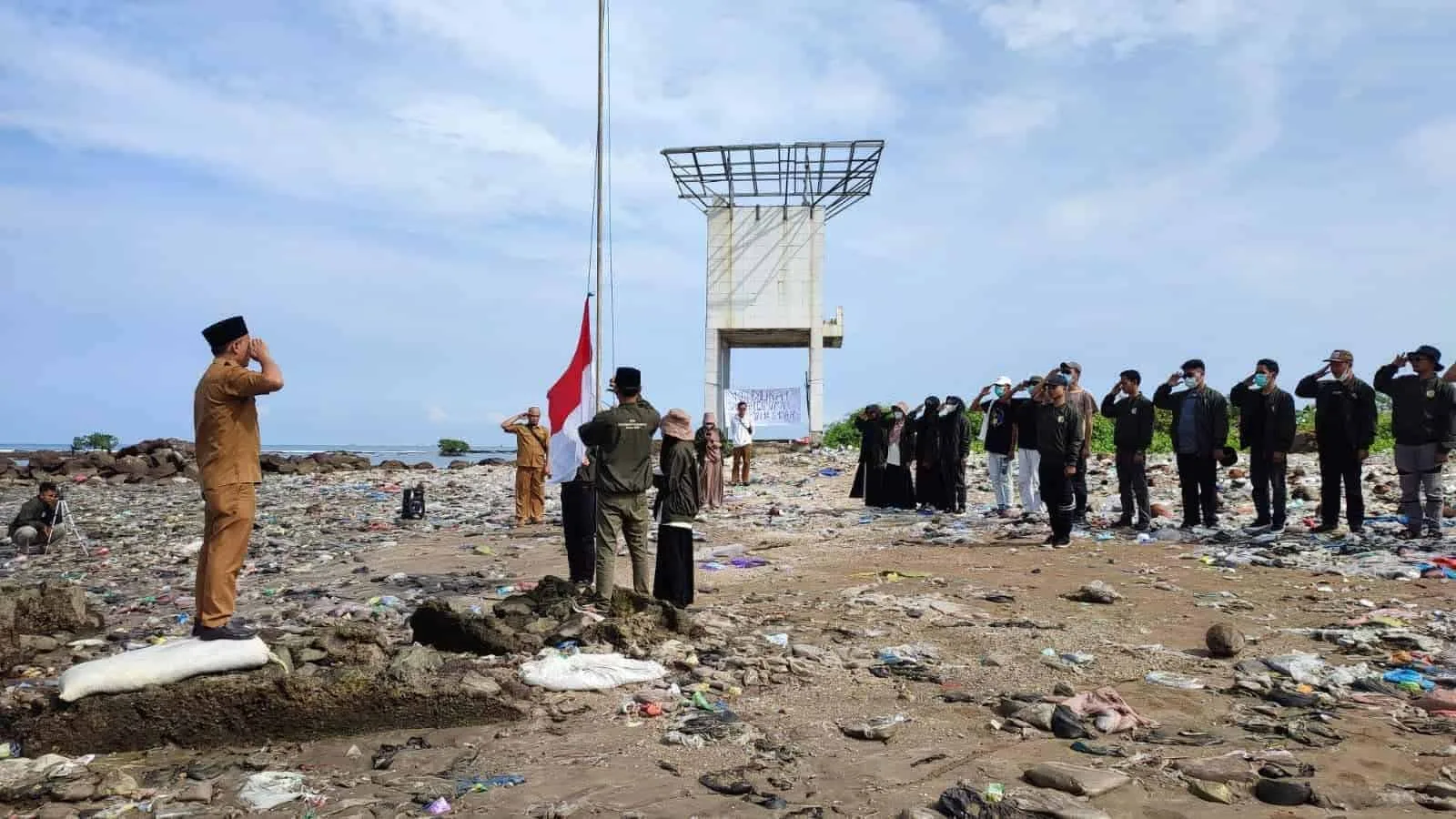 Para mahasiswa KKN STAISMAN Pandeglang, bersama aparatur Desa Teluk, sedang upacara diatas tumpukan sampah di Pantai Teluk Labuan, Senin (22/8/2022). (ISTIMEWA)