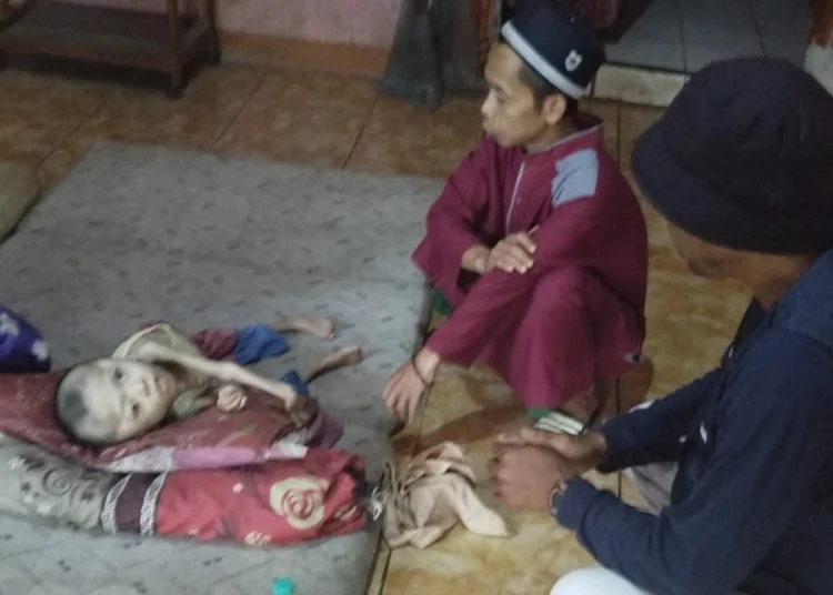 Dudu (8), warga Pandeglang terlihat berbaring di depan ayahnya. Ia sudah menderita gizi buruk, sejak 8 tahun lalu. (ISTIMEWA)